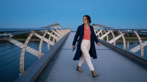 Baha Meier Arian geht in einem kobaltblauen Mantel über eine moderne Brücke.