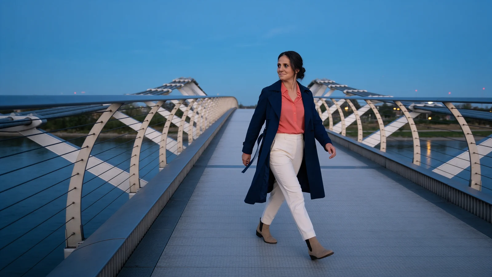 Baha Meier Arian geht in einem kobaltblauen Mantel über eine moderne Brücke.